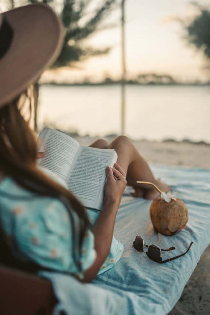 woman in blue and white floral dress reading book on beach